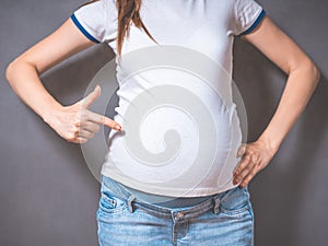 Pregnant woman holds hands on belly on a gray background.