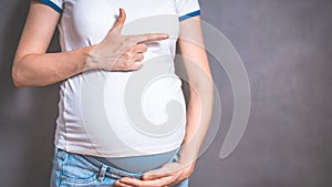 Pregnant woman holds hands on belly on a gray background.