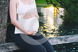 Pregnant woman holds hands on belly on nature background