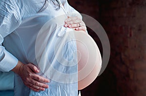 Pregnant woman holds hands on her belly, close-up.