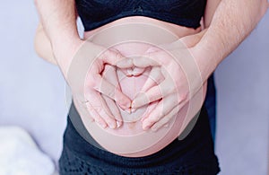 Pregnant woman holds hands on her belly, close-up. Mother waiting for baby.