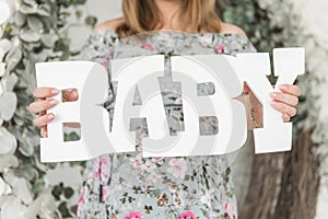 A pregnant woman holds in her hands the big white letters