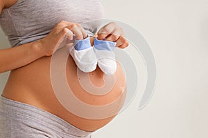 A pregnant woman holds a pair of baby shoes in front of her pregnant belly