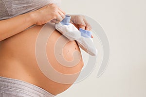 A pregnant woman holds a pair of baby shoes in front of her pregnant belly