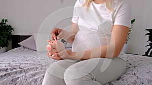 A pregnant woman holds a pig bank in her hands. Selective focus.