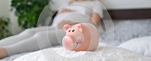 A pregnant woman holds a pig bank in her hands. Selective focus