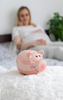 A pregnant woman holds a pig bank in her hands. Selective focus