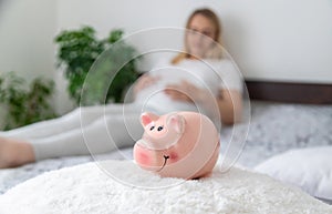 A pregnant woman holds a pig bank in her hands. Selective focus