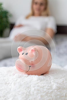 A pregnant woman holds a pig bank in her hands. Selective focus