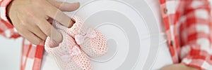 Pregnant woman holds pink baby slippers on stomach closeup