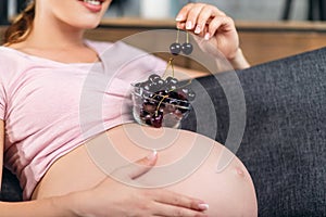 The pregnant woman holds a plate with cherry.