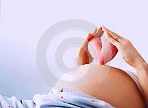 Pregnant woman holds symbol in heart shape. Loving mother waiting of baby. Concept of maternity, pregnancy, prepare and expect