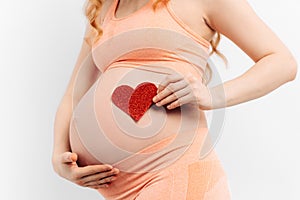 Pregnant woman holds a symbol in the shape of a heart in her palms on a white background