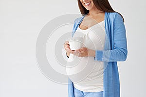 Pregnant woman holing a cup of tea isolated over white background