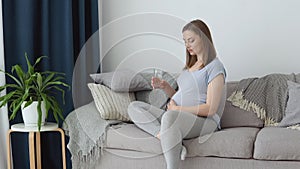 Pregnant woman in home clothes sitting on the couch holding a glass of water in her hands. Third trimester of pregnancy