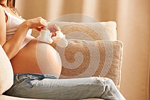 Pregnant woman at home holding small baby shoes