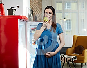 Pregnant woman at home in kitchen with fridge