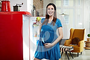 Pregnant woman at home in kitchen with fridge