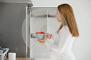 Pregnant woman at home in the kitchen opens the refrigerator