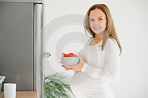 Pregnant woman at home in the kitchen opens the refrigerator