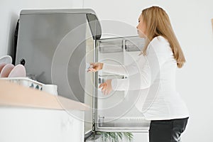 Pregnant woman at home in the kitchen opens the refrigerator