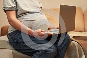 Pregnant woman at home is sitting with computer, online shopping or home office