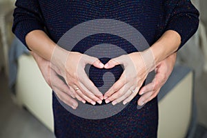 Pregnant woman hugging her husband. Hands folded on his belly in the form of the heart symbol birth of new life