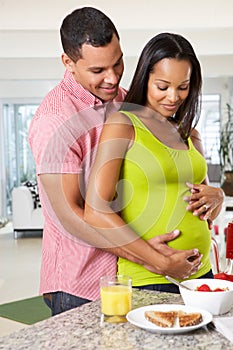 Pregnant Woman And Husband Having Breakfast In Kitchen