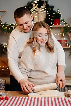 pregnant woman with husband in New Year kitchen roll out dough with rolling pin