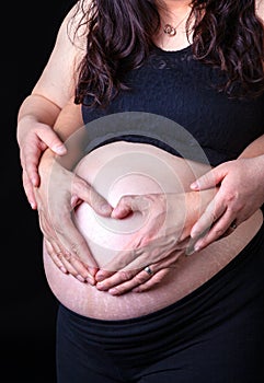 Pregnant Woman With Husband`s Hands With Love Symbol on Tummy