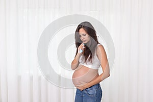 Pregnant woman in jeans and white top in bedroom. Pregnancy health and medcine contest. Illness, flu, allergy photo
