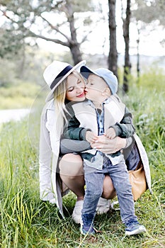 Pregnant woman with kid outdoors. Mother and her son on nature in spring forest. Little child boy kissing mother, who pregnant for