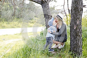 Pregnant woman with kid outdoors. Mother and her son on nature in spring forest. Little child boy kissing mother, who pregnant for