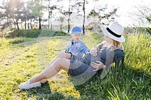 Pregnant woman with kid outdoors. Mother and her son on nature in spring forest. Little child boy and mother, who pregnant for