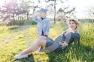 Pregnant woman with kid outdoors. Mother and her son on nature in spring forest. Little child boy and mother, who pregnant for