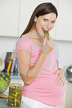 Pregnant woman in kitchen eating pickles