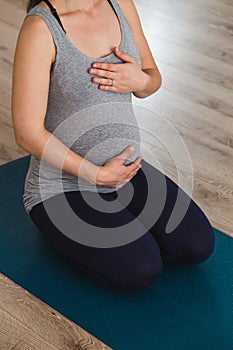 Pregnant woman kneeling on yoga mat with hands on heart and belly doing prenatal yoga