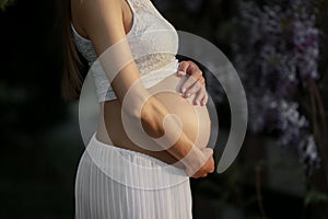 A pregnant woman in late term pregnancy in the garden of Wisteria in bloom hugs the belly