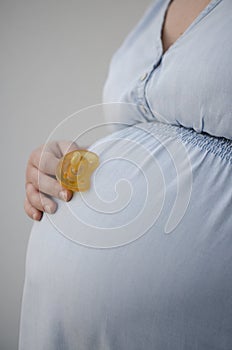 Pregnant woman in light blue denim dress holding pacifier