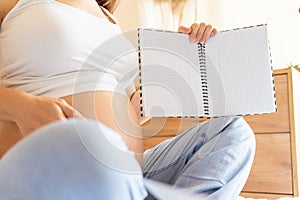 Pregnant woman list. Young pregnancy mother holding notepad. Pregnant lady writing check list of baby. Pregnancy