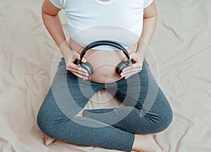 Pregnant woman listen to music with headphone on tummy