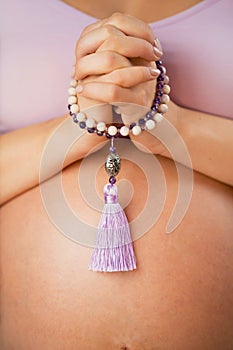 Pregnant woman, lit hand close up, counts Malas, strands of gemstones beads used for keeping count during mantra