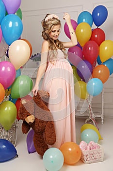 Pregnant woman with long blond hair in elegant dress, with a lot of colorful air balloons