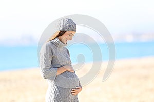 Pregnant woman looking at belly on the beach in winter