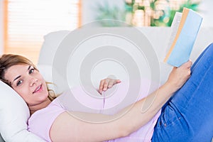 Pregnant woman looking at camera and reading a book