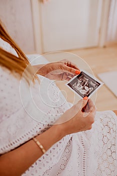 Pregnant woman looking at her baby twins sonography. Happy expectant mother enjoying first photo of her kids, face is