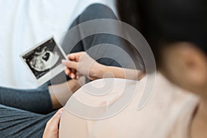 A pregnant woman is looking at an ultrasound photo of fetus. Mother gently touches the baby on stomach.Women are pregnant for 30 w
