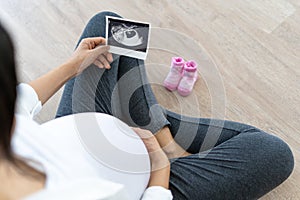 A pregnant woman is looking at an ultrasound photo of fetus. Mother gently touches the baby on stomach.Women are pregnant for 30 w