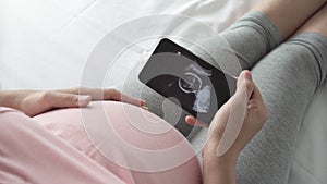 Pregnant woman looking ultrasound photo on Smartphone