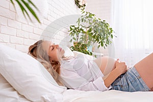 Pregnant woman is lying on bed on her back. Stroking her bare belly. childbirth